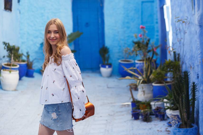 Beautiful woman in white top and jeans skirt exploring the blue street of Morocco