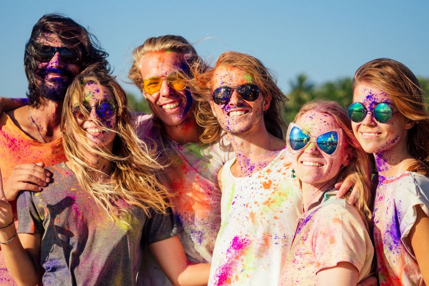 mixed race friends having fun with colors on seaside outdoors in Goa India