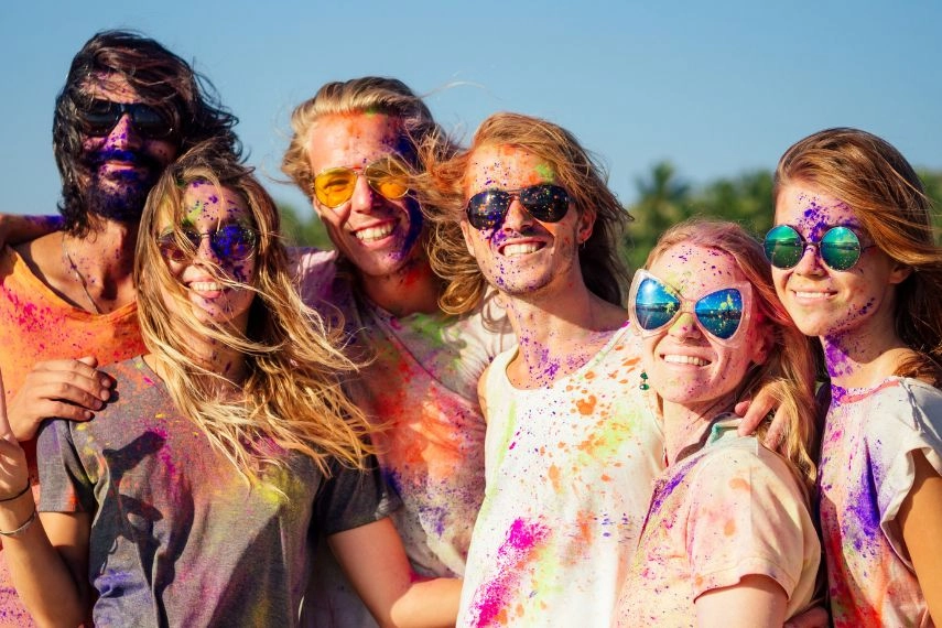 mixed race friends having fun with colors on seaside outdoors in Goa India
