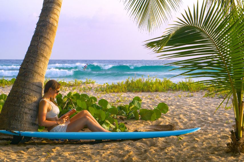 Woman relaxes on the beach near a popular surf spot and reads a book in Barbados