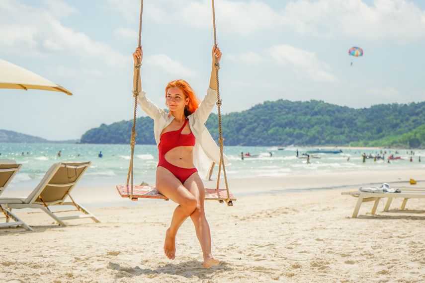 Long red haired woman sitting on the swing on the tropical Bai Sao beach on Phu Quoc island, Vietnam