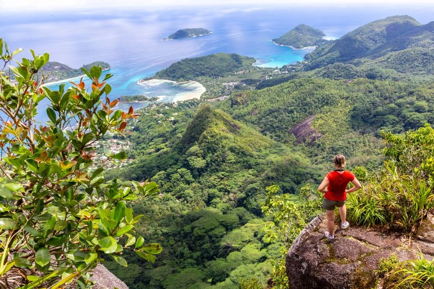 Young female traveller standing at the edge of the cliff at Morne Blanc View Point, overlooking Mahe Island coastline
